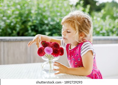 Portrait Of Little Toddler Girl Admiring Bouquet Of Blooming Red And Pink Dahlia Flowers. Cute Happy Child Smelling And Counting Flower On Sunny Summer Day.