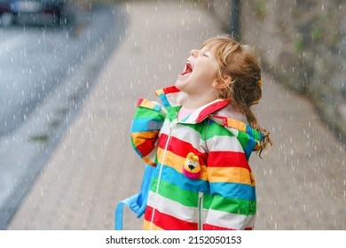 Portrait of little toddler girl on rainy day. Happy positive child running through rain, puddles. Preschool kid with rain clothes catching rain drops. Children activity on bad weather day.