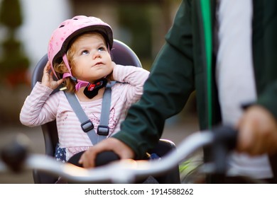 Portrait Of Little Toddler Girl With Security Helmet On The Head Sitting In Bike Seat And Her Father Or Mother With Bicycle. Safe And Child Protection Concept. Family And Weekend Activity Trip.