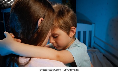 Portrait of little upset and sad toddler boy hugging and kissing his mother before going to sleep at night. Loving and caring parents and children.