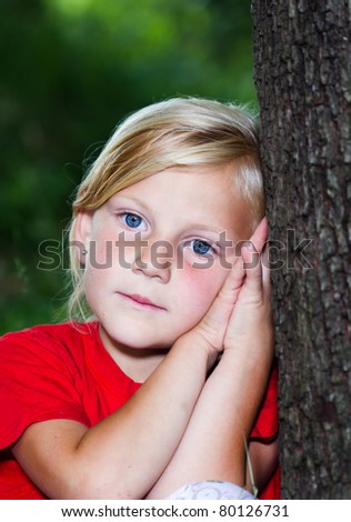 Portrait of little worried t girl leaning against a tree in forest