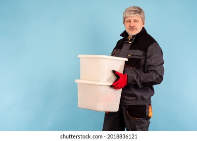 Portrait of a loader with boxes in his hands. Loader on a blue background. Man in the uniform of a loader with plastic containers. Place for inscription next to worker. Warehouse or factory worker