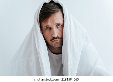 Portrait Of A Lonely Sad Adult Man With Symptoms Of Depression And Melancholy, Wrapped With A Blanket Over His Head, Looking Sadly At The Camera. Male Mental Health Concept.