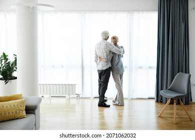 Portrait Of A Lonely  Senior Couple Embracing Hugging And Looking Through Window At Home