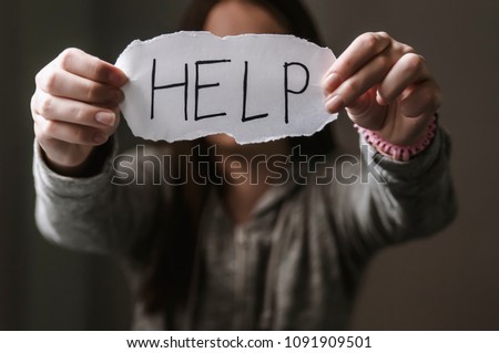 Portrait of lonely teenage girl sitting alone with depressed expression and showing a paper with a help text. Violence against women