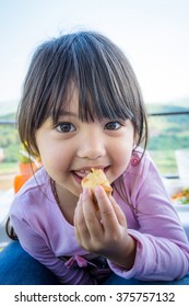 A Portrait Of Long Hair Pretty Little Girl Eating Crispy Spring Roll Laying On Mother And Blurry Mountain And Sky Background