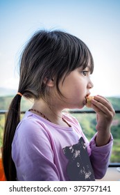 A Portrait Of Long Hair Pretty Little Girl Eating Crispy Spring Roll With Blurry Mountain And Sky Background