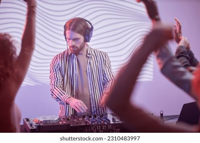 Portrait of long haired DJ by turntable in neon lights entertaining dancing crowd at disco party - Shutterstock ID 2310483997