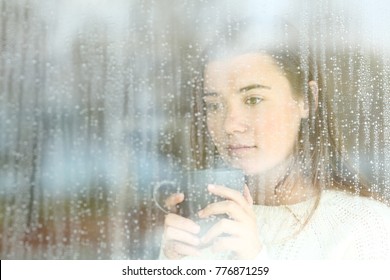 Portrait Of A Longing Teen Looking Through A Window Alone At Home In A Rainy Day