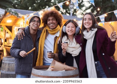 Portrait looking camera of Happy friends eating chocolate with churros street food stall at the city outdoors. Tourist group of four people having fun in a terrace cafeteria in winter time.  - Powered by Shutterstock