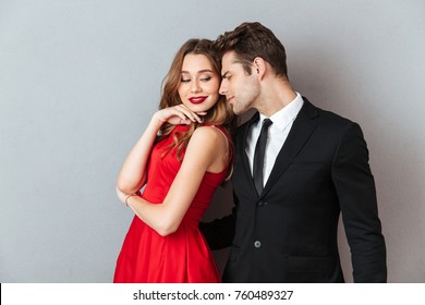 Portrait Of A Lovely Attractive Couple Dressed In Formal Wear Posing While Standing And Hugging Over Gray Wall Background