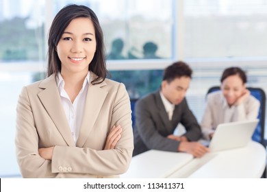 Portrait Of A Lovely Business Lady, The Embodiment Of Enthusiasm And Success, Her Colleagues Working In The Background