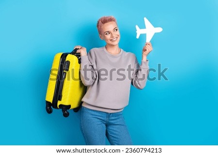Portrait of lovely cheerful person toothy smile arm hold suitcase small paper plane isolated on blue color background