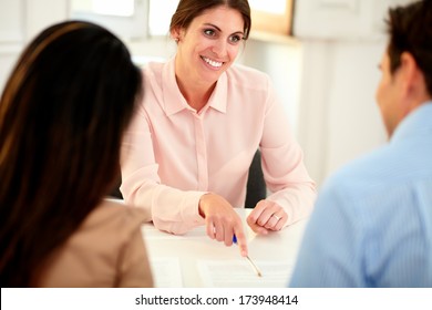 Portrait Of Lovely Financial Advisor Woman At Meeting With Young Couple While Smiling And Sitting At Bank Office