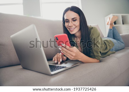 Portrait of lovely focused cheerful girl lying on divan bare foot using laptop device blogging smm at home house flat indoor