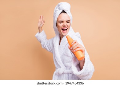 Portrait of lovely funky cheerful girl wear bathrobe singing using shampoo like mic fooling isolated over beige pastel color background