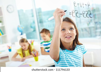 Portrait of lovely girl doing sums on transparent board with two schoolmates on background - Powered by Shutterstock