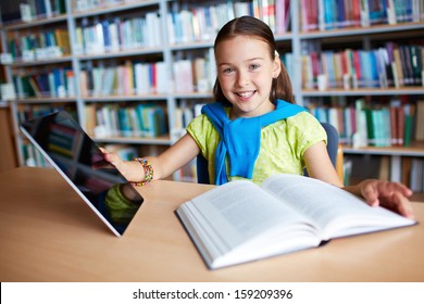 Portrait of a lovely girl with touchpad and open book sitting in library - Powered by Shutterstock