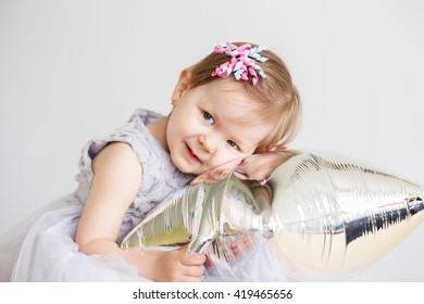 Portrait of a lovely little girl in elegant gray dress in front of a white background. Little princess. Little baby girl playing with silver star-shaped balloon.