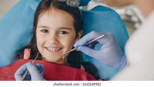 Portrait of a lovely little girl looking at camera smiling while sitting in a pediatric stomatology after teeth examination.