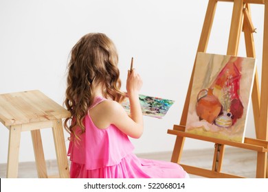 Portrait Of A Lovely Little Girl Painting A Picture In A Studio Or Art School. Creative Pensive Painter Child Paints A Colorful Picture On Canvas With Oil Colors In Workshop. Talented Kids