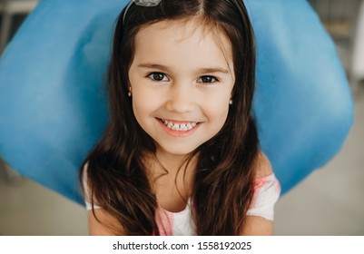 Portrait of a lovely little girl sitting in a pediatric stomatology looking at camera laughing before teeth surgery.