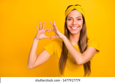 Portrait of lovely millennial making heart form with her hands smiling wearing t-shirt isolated over yellow background