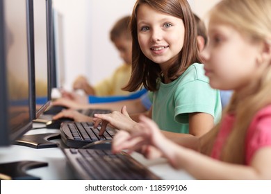 Portrait of lovely schoolgirl looking at camera while typing at lesson