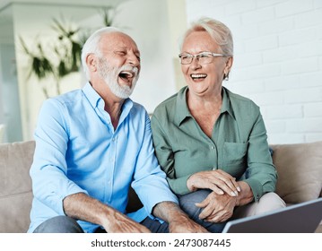 Portrait of a lovely senior mature couple using a laptop together and having fun sitting on sofa at home - Powered by Shutterstock