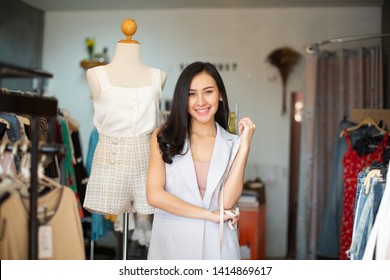 Portrait of a lovely shop owner standing near the rack of clothes hangings on the foreground - Powered by Shutterstock