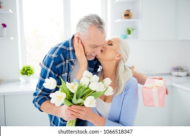 Portrait of lovely sweet attractive stylish joyful glad modern woman kissing her lover in cheek because he prepared surprise, bouquet of tulips, packed case for her, celebrating valentine day - Powered by Shutterstock