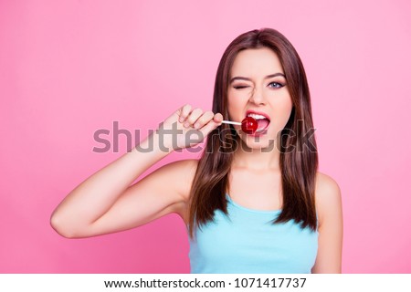 Portrait of lovely sweet cute charming beautiful cheerful hungry adorable gorgeous woman with straight brown hair trying to bite red lollipop  on stick, isolated on bright pink background