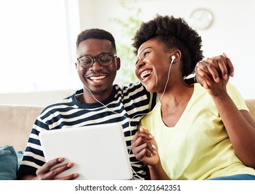 Portrait of a lovely young couple having fun and listening music wearing earphones and holding tablet together at home - Powered by Shutterstock