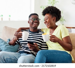 Portrait of a lovely young couple having fun, drinking coffee or tea and using smartphone together at home - Powered by Shutterstock