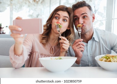 Portrait of a lovely young couple taking a selfie while having lunch together at the cafe table indoors - Powered by Shutterstock