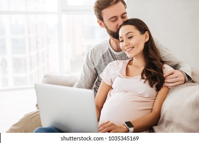 Portrait of a lovely young pregnant couple sitting on a couch with laptop computer