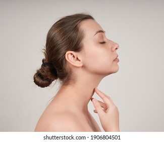 Portrait Of Lovely Young Woman In Profile With Bare Shoulders, Touching Her Neck. Studio Shot On Light Background