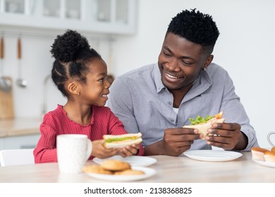 Portrait Of Loving Black Family Single Father And Little Daughter Having Lunch Together At Home, Dad And Kid Sitting At Kitchen Table, Eating Sandwiches, Drinking Tea, Having Conversation And Smiling