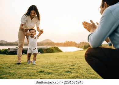 Portrait of a loving family spending quality time in nature, teaching their baby girl to walk on a beautiful spring day. childhood parent care support concept - Powered by Shutterstock