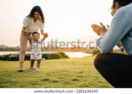 Portrait of a loving family spending quality time in nature, teaching their baby girl to walk on a beautiful spring day. childhood parent care support concept