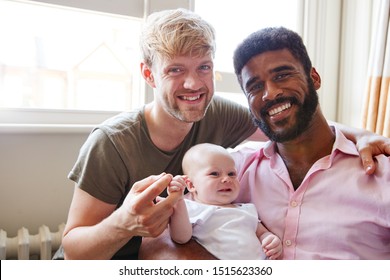 Portrait Of Loving Male Same Sex Couple Cuddling Baby Daughter On Sofa At Home Together