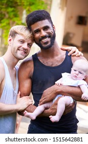 Portrait Of Loving Male Same Sex Couple Cuddling Baby Daughter At Home In Garden Together