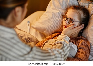 Portrait Of Loving Mother Caring For Sick Child With Down Syndrome Suffering From Fever At Night In Warm Lamplight