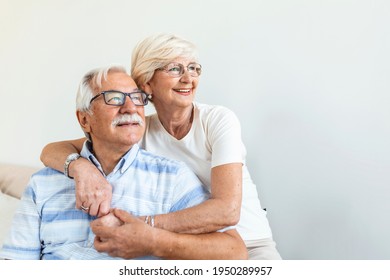 Portrait Loving Older Wife Hugging Husband Sitting On Cozy Couch. Happy Senior Mature Couple Smilling And Looking At Camera, Posing For Family Photo At Home. Elderly Couple Feeling Happy