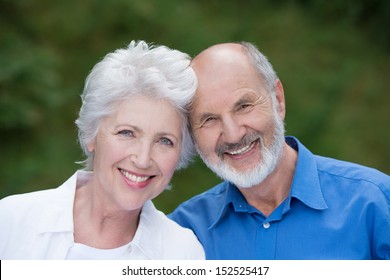 Portrait Of A Loving Senior Couple Standing Together Outdoors Facing The Camera And Smiling With Their Heads Touching