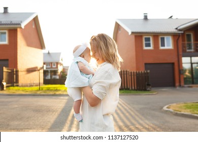 Portrait of loving young mother playing with her kid in evening in front of house. Playful woman holding little cute daughter above her head. Calm caring mommy smiling through the rays of sunset