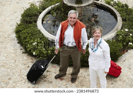 Portrait, luggage and senior couple at hotel, water fountain or holiday vacation from above. Smile, elderly man and woman with suitcase at courtyard outdoor for tourism, travel or retirement together