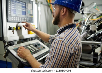 Portrait of machine operator wearing hardhat standing at control panel pressing buttons, copy space