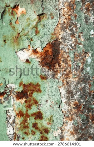 Portrait macro of green paint cracking and peeling extensively over a rust-covered metal surface, revealing layers of orange, brown, and gray beneath. Rich in color and detail, ideal for industrial and decay-themed design.