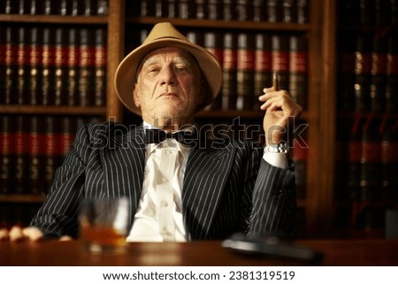 Portrait, mafia and boss with cigarette in office for habit, smoking or relaxing by desk. Mature, mob leader and retro fashion in suit, bowtie and hat for crime, danger or power with vintage look